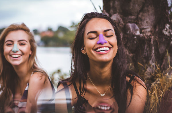 Two women outside smiling while wearing different shades of Noz water-resistant sunscreen lotion, in seafoam and lavender