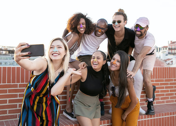 Group of friends outdoors posing for a selfie, each wearing a different color of Noz non toxic sunscreen 