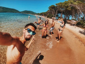 Friends at the beach in the water and posing for a selfie, each sporting a different shade of Noz coral reef safe sunscreen